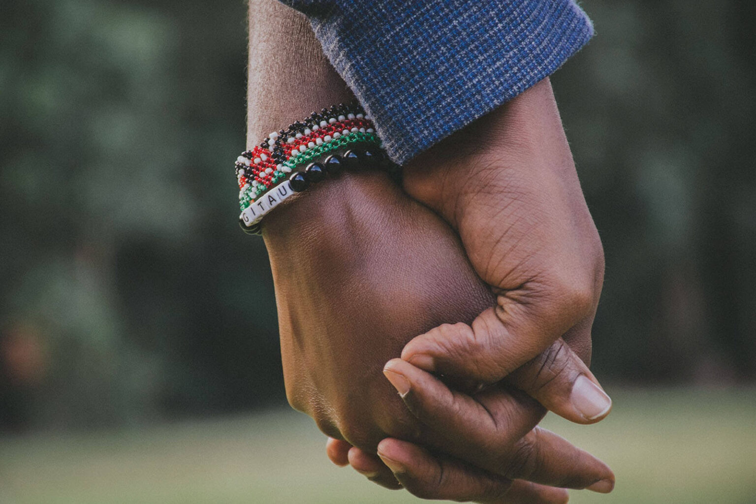 A close-up of two people holding hands, one wearing colourful beaded bracelets, with a blurry background that highlights the connection between their hands