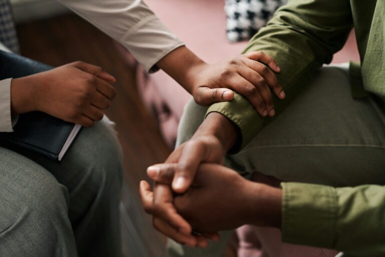 One person holds another's arm, offering comfort, while both are seated.